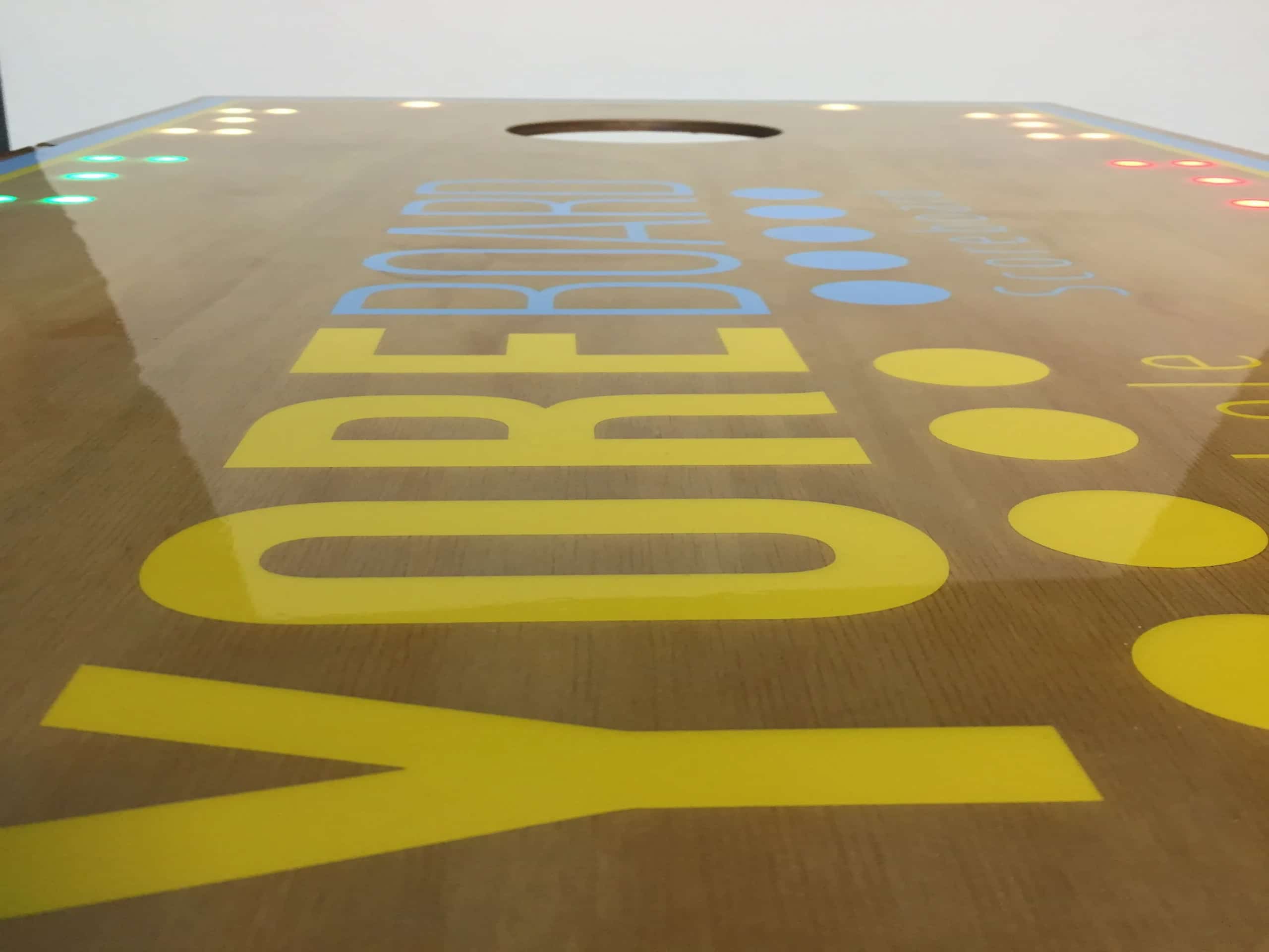 Dramatic view of a resin YoreBoard cornhole surface, highlighting its distinctive logo and the vibrant array of active Scoring LEDs.