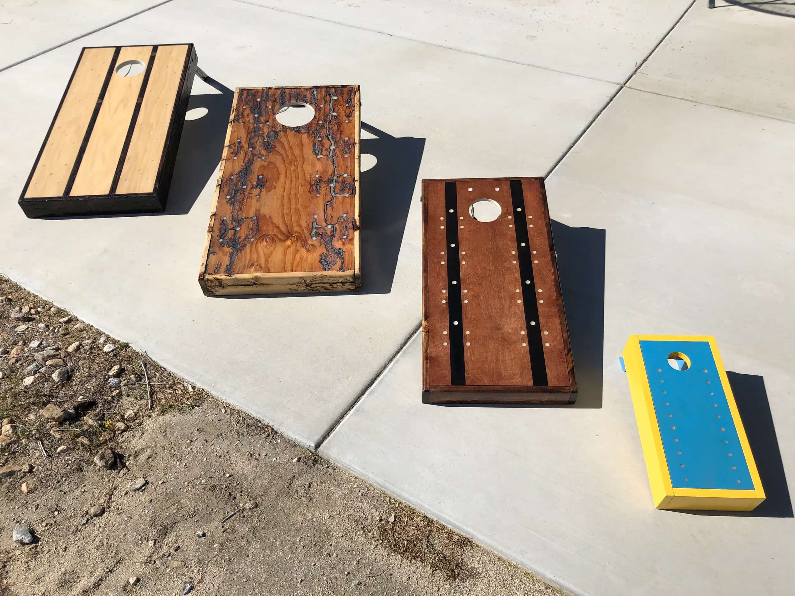 Various YoreBoard prototype cornhole boards demonstrating different design iterations, wood finishes, and layouts for Scoring LEDs, set outdoors.