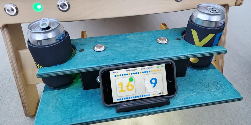 Interactive YoreBoard score box with integrated smartphone/tablet holder for real-time digital scoring, alongside convenient beverage holders and scoring buttons.