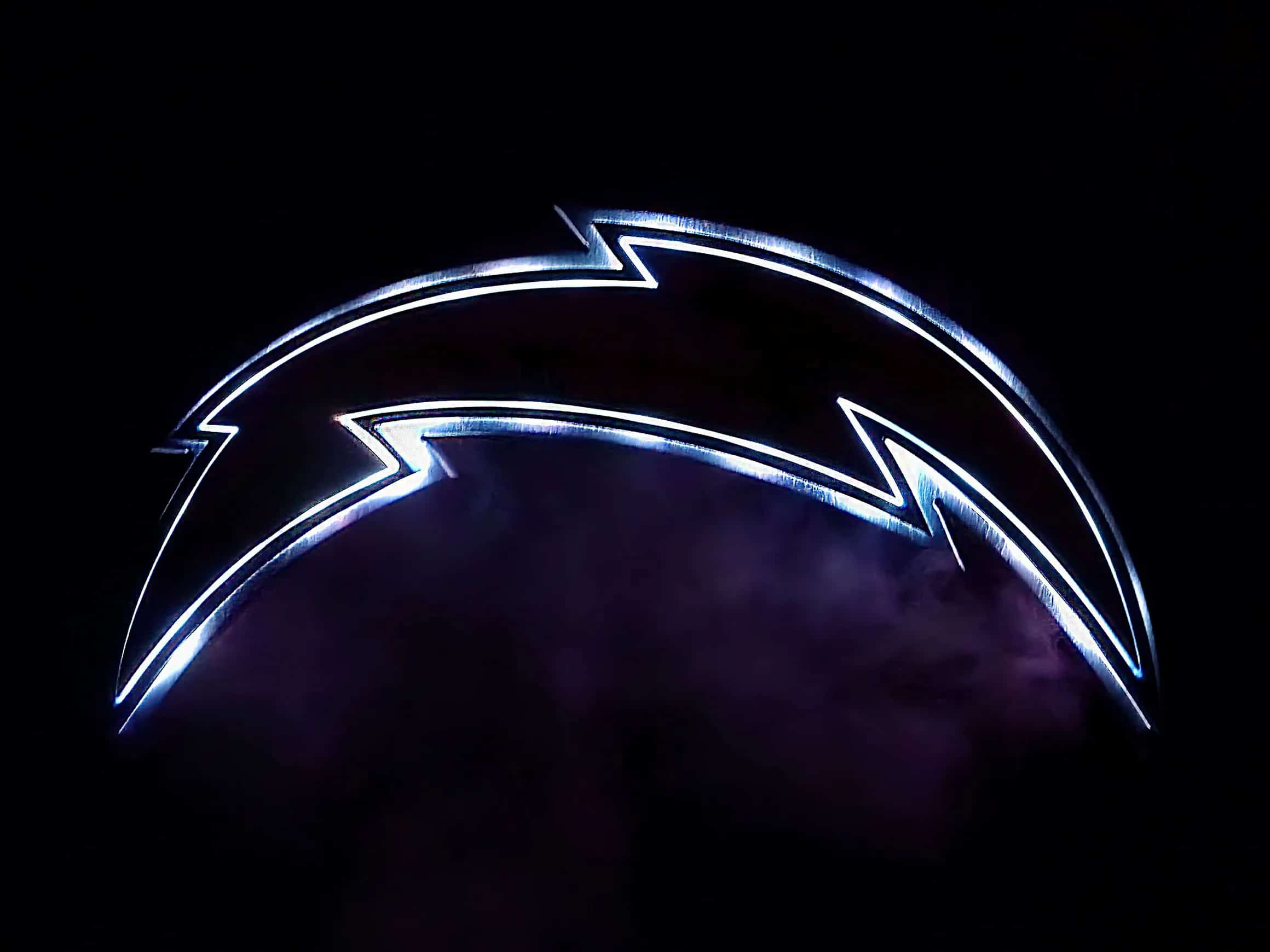 Illuminated Los Angeles Chargers lightning bolt logo, glowing with bright white and subtle blue light, creating a neon effect against a dark, possibly smoky, background. The light outlines the iconic bolt shape.